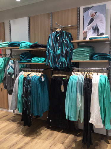 Regale mit grünen Pullovern, Blusen und Hosen, gemusterte Bluse und Poster mit Wintermode.